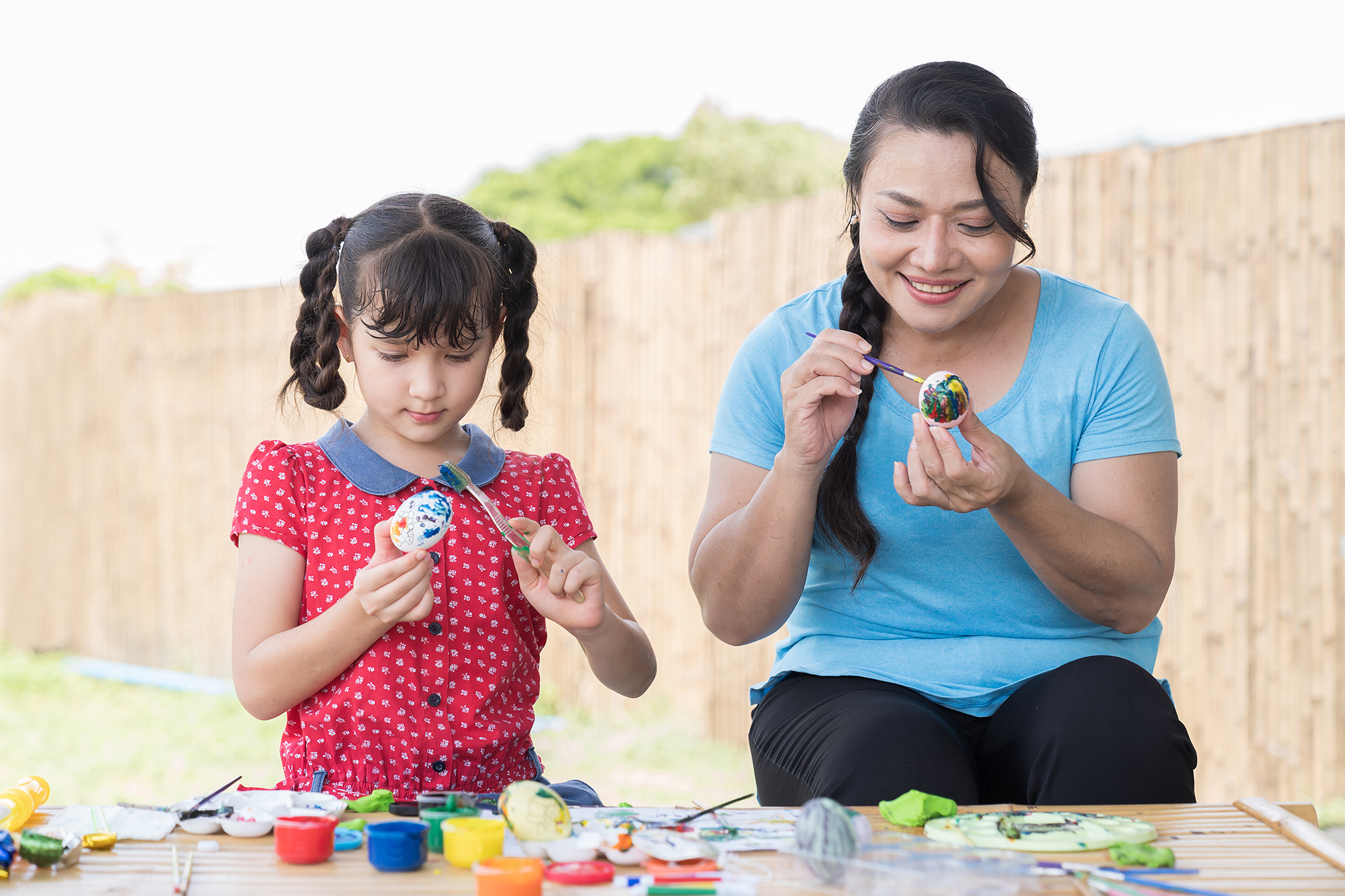 Smiling adult woman and child girl painting eggs with brush and sculpts modeling clay multi-colored plasticine class in workshop