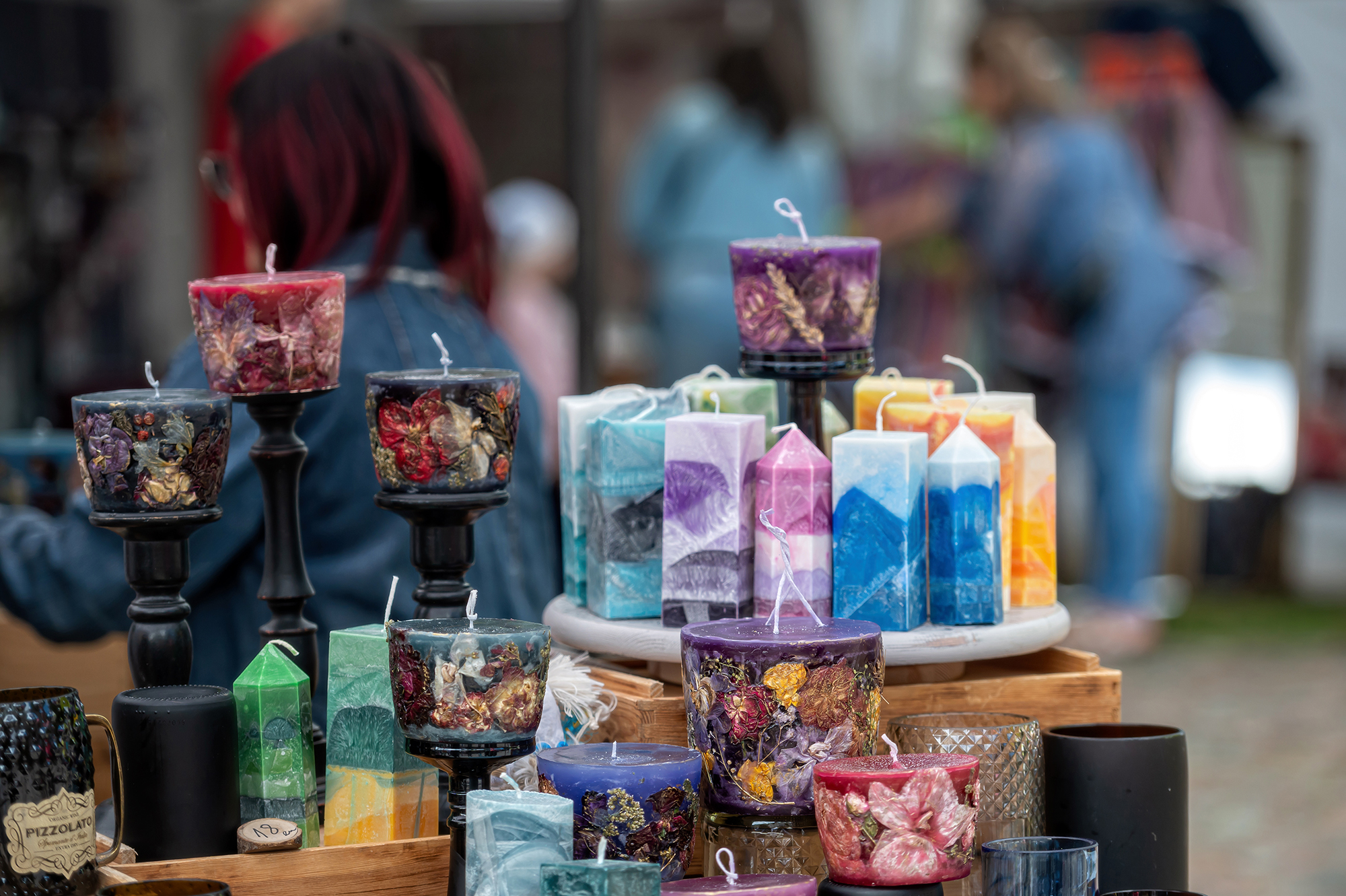 A variety of candles are displayed for sale at a craft market. Shallow depth of feld