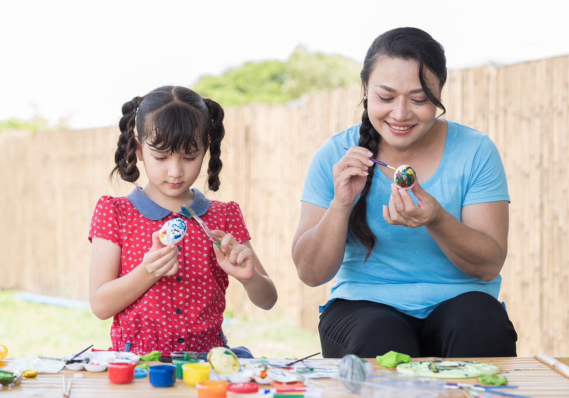 Smiling adult woman and child girl painting eggs with brush and sculpts modeling clay multi-colored plasticine class in workshop