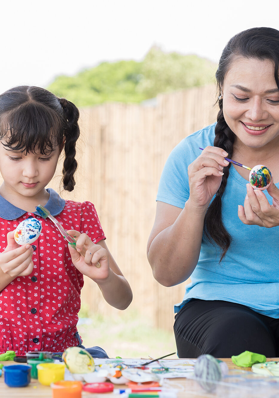 Smiling adult woman and child girl painting eggs with brush and sculpts modeling clay multi-colored plasticine class in workshop