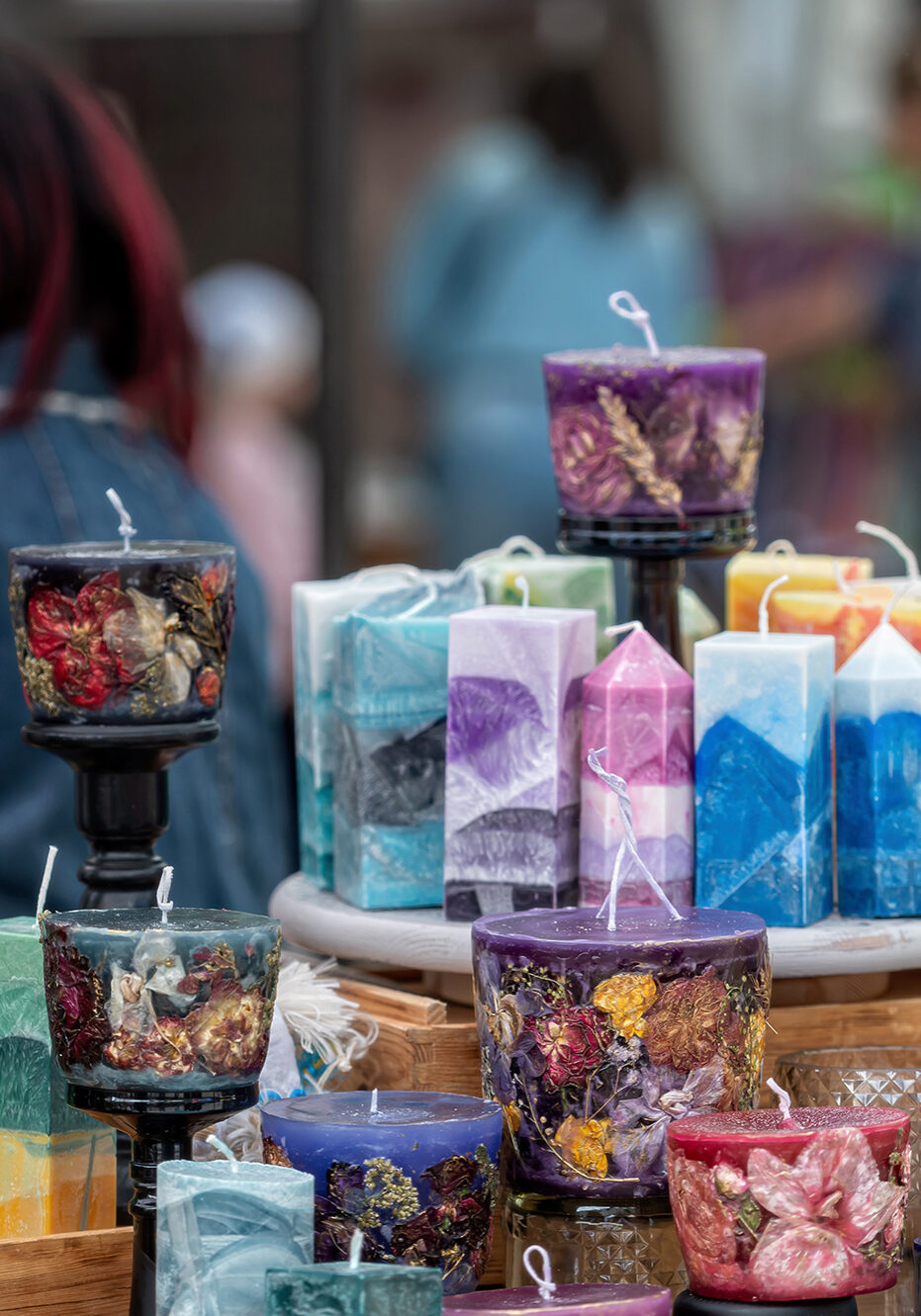 A variety of candles are displayed for sale at a craft market. Shallow depth of feld